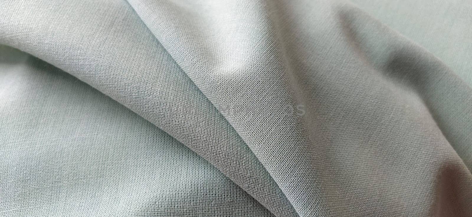 white fabric with interlacing threads close-up. Light green tint. Nice beautiful waves on the material. A neatly folded piece of fabric. Interior decoration, tailoring. Textile industry.