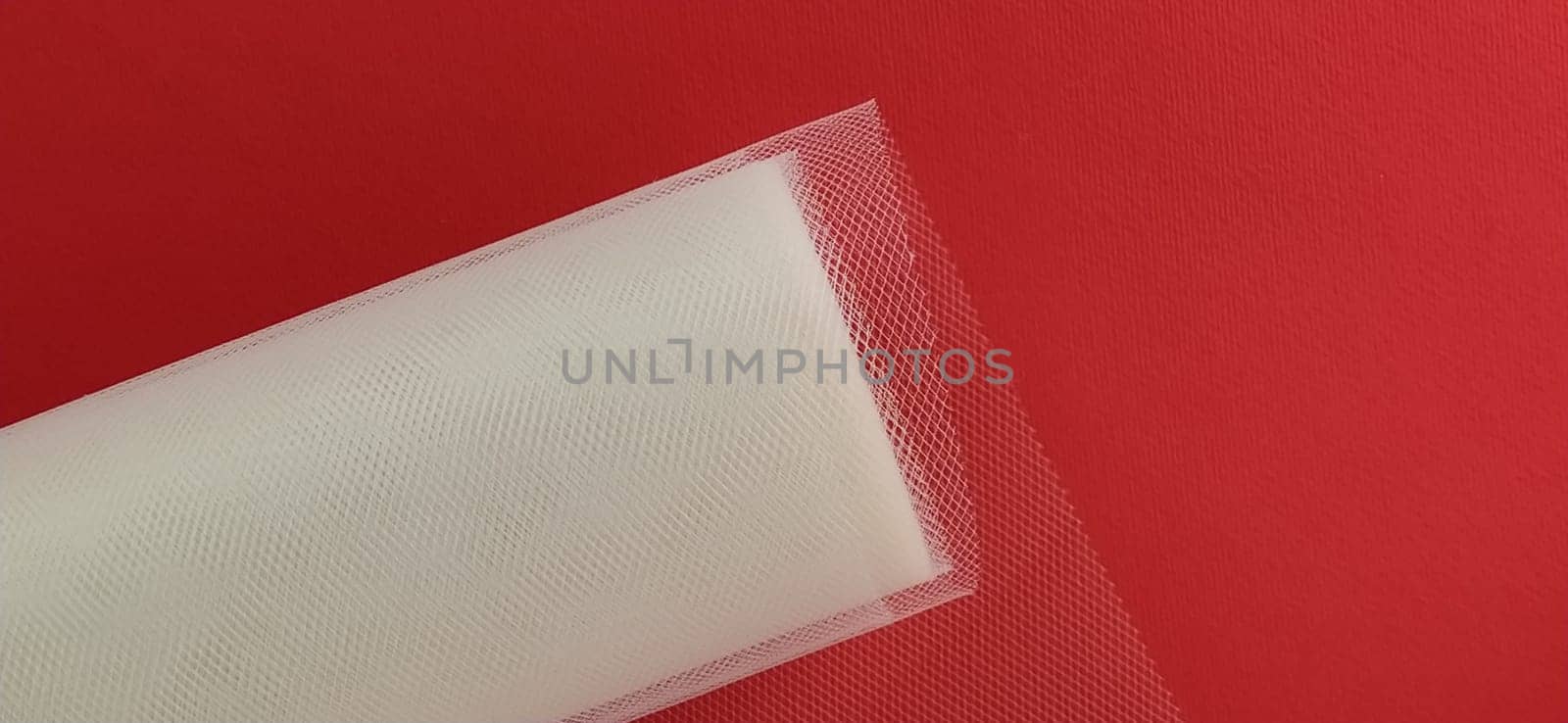 Fabric - white mesh in a roll on a red background. Nylon tape for tying bows on hair. A skein of tulle fabric. Copy space.