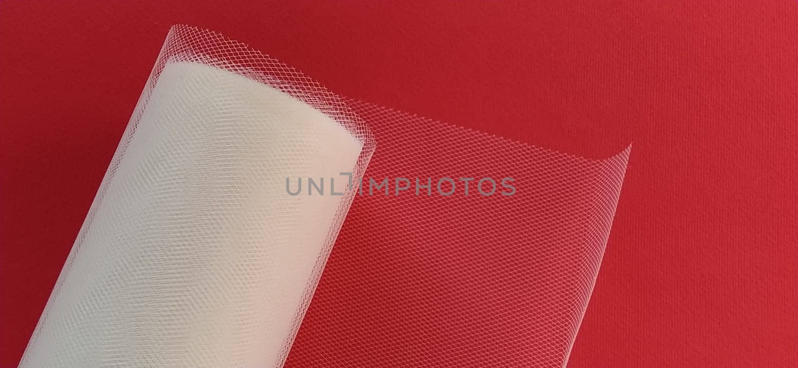 Fabric - white mesh in a roll on a red background. Nylon tape for tying bows on hair. A skein of tulle fabric. Copy space.
