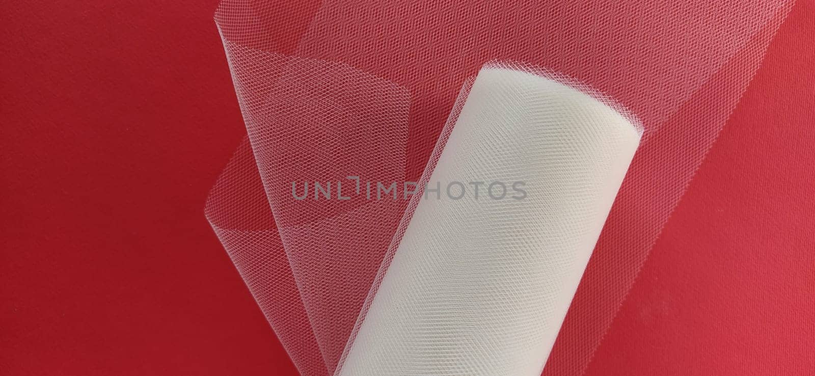 Fabric - white mesh in a roll on a red background. Nylon tape for tying bows on hair. A skein of tulle fabric. Copy space.