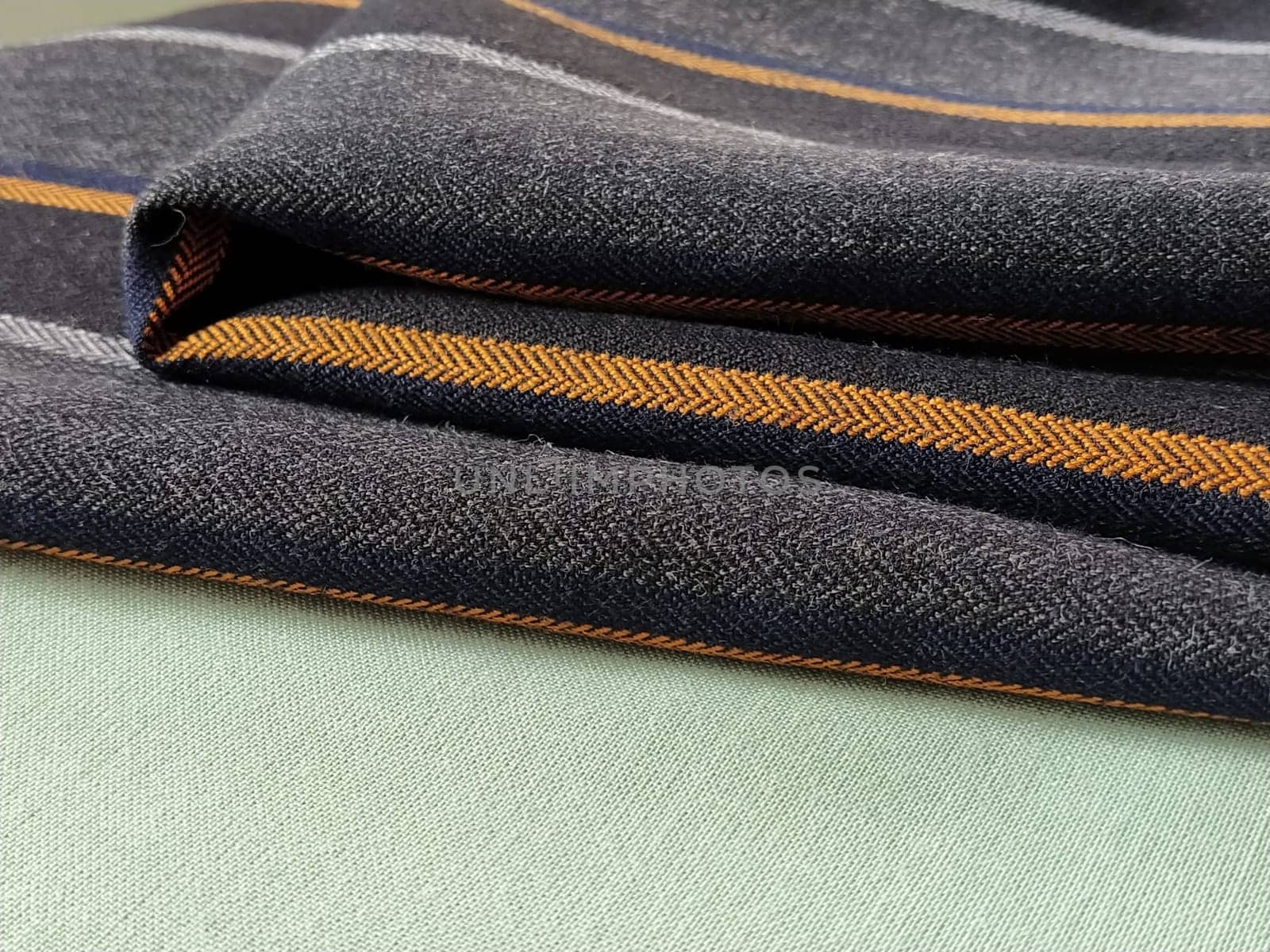 Gray-black fabric with orange and blue stripes. Textile fabric folded neatly on the surface. Natural wool material for sewing clothes and upholstery. Lifestyle. Close-up. Soft focus.