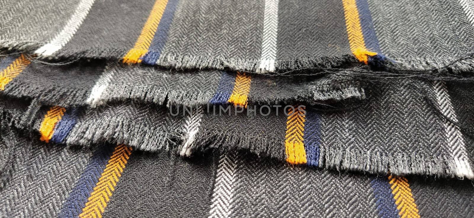 Light black-gray folded fabric with orange and dark blue stripes. Ripped, unfinished fabric edge. Interior decoration. Dress fabrics in casual style. Dense material for furniture finishing.
