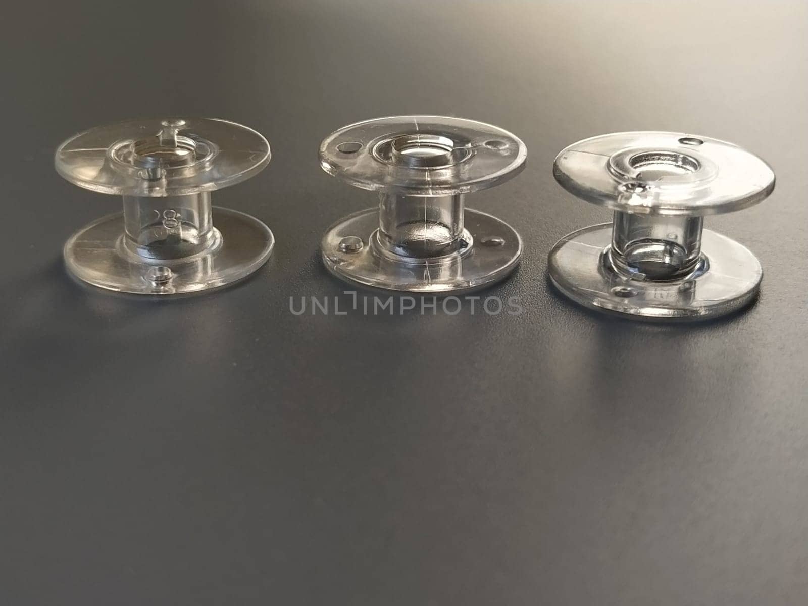 Three transparent plastic sewing machine bobbins. Textile industry. Detail of sewing equipment. Gray background, back lighting.