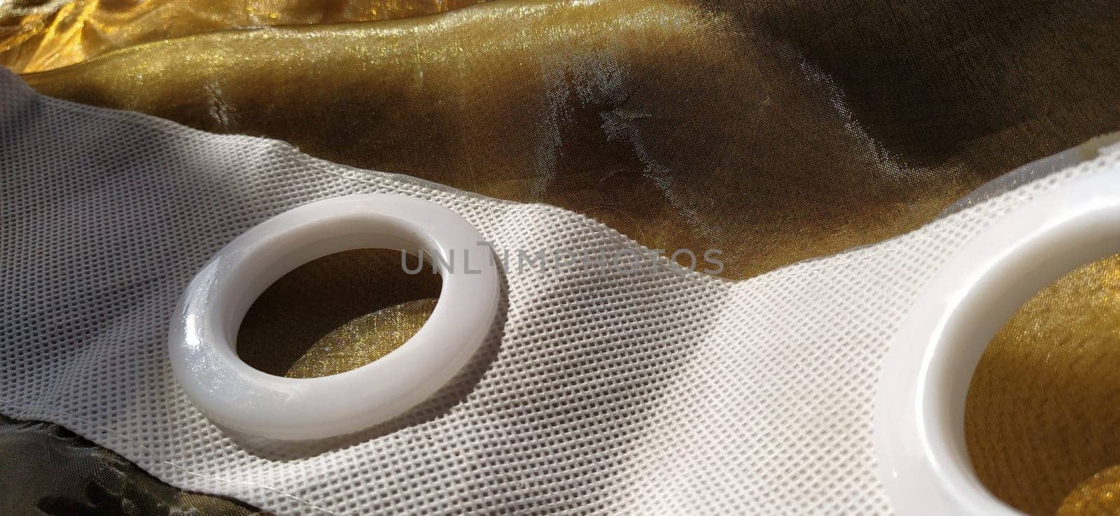 Plastic rings for attaching the fabric to the curtain rod. White plastic organza tulle eyelets. Light curtain in beige, brown or orange colors. White non-woven fabric. Finished textile edge. Interior element