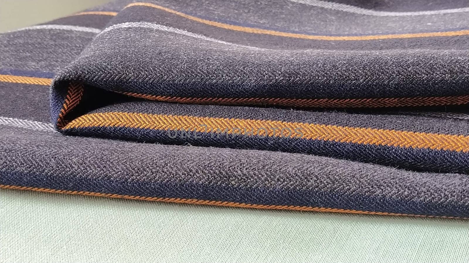 Gray-black fabric with orange and blue stripes. Textile fabric folded neatly on the surface. Natural wool material for sewing clothes and upholstery. Lifestyle. Close-up. Soft focus.