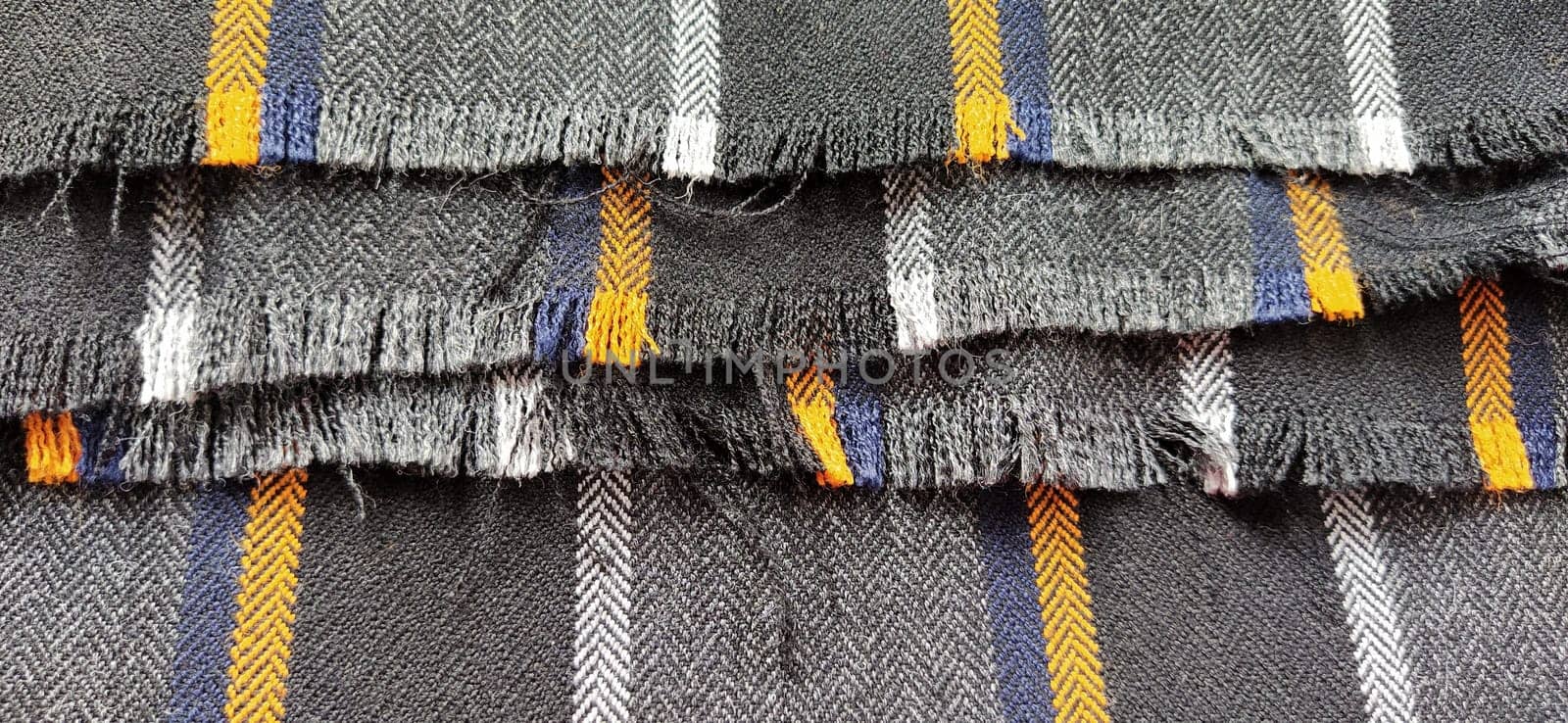 Light black-gray folded fabric with orange and dark blue stripes. Ripped, unfinished fabric edge. Interior decoration. Dress fabrics in casual style. Dense material for furniture finishing.