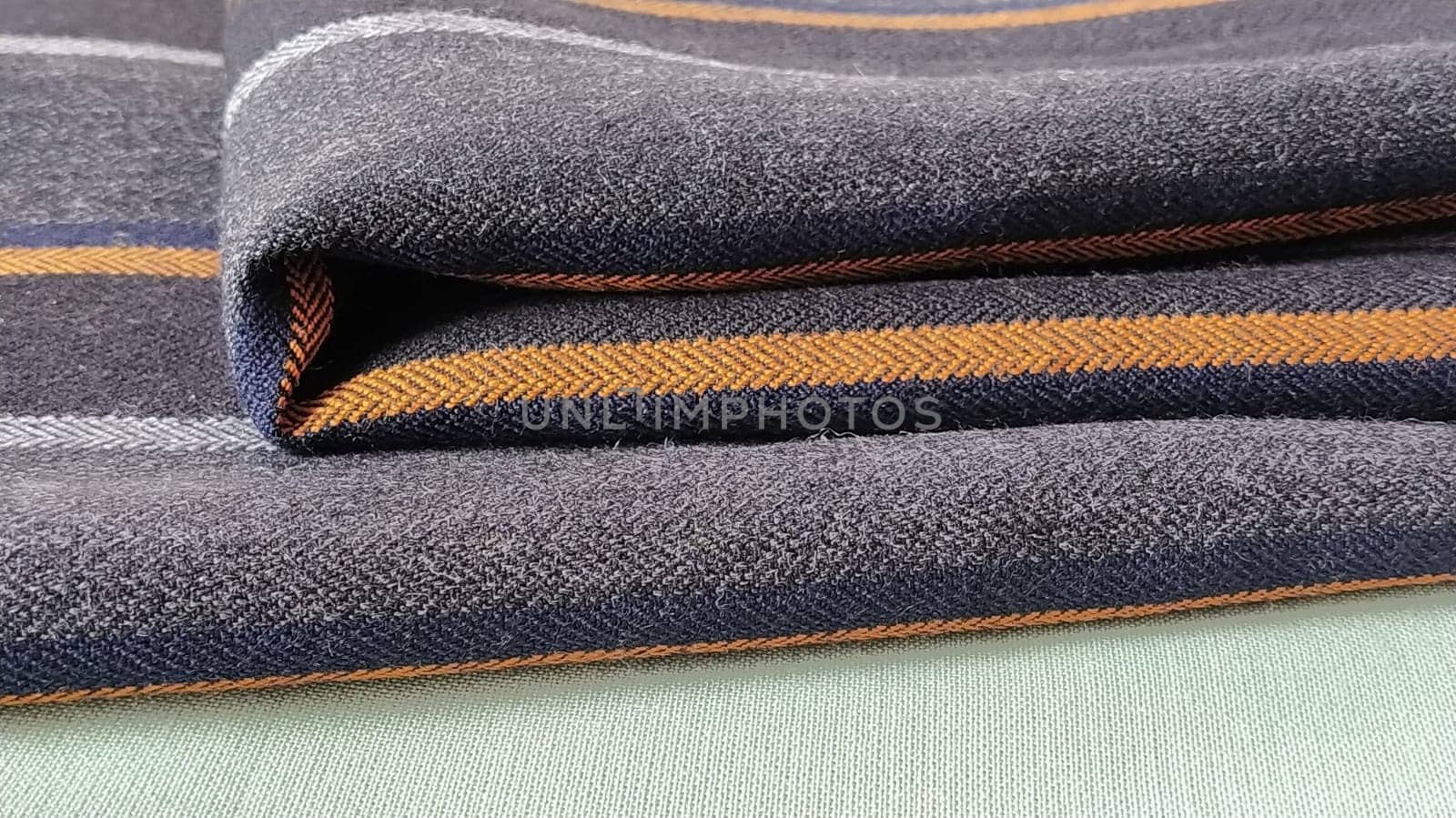 Light green and black-gray folded fabric with orange and dark blue stripes. Interior decoration. Dress fabrics in casual style. Dense material for indoor curtains and furniture finishing.