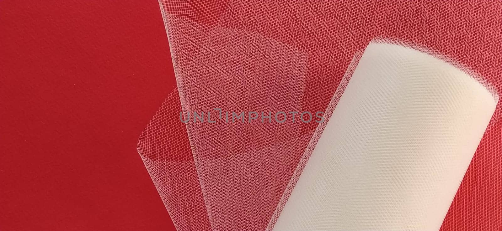 Fabric - white mesh in a roll on a red background. Nylon tape for tying bows on hair. A skein of tulle fabric. Copy space.