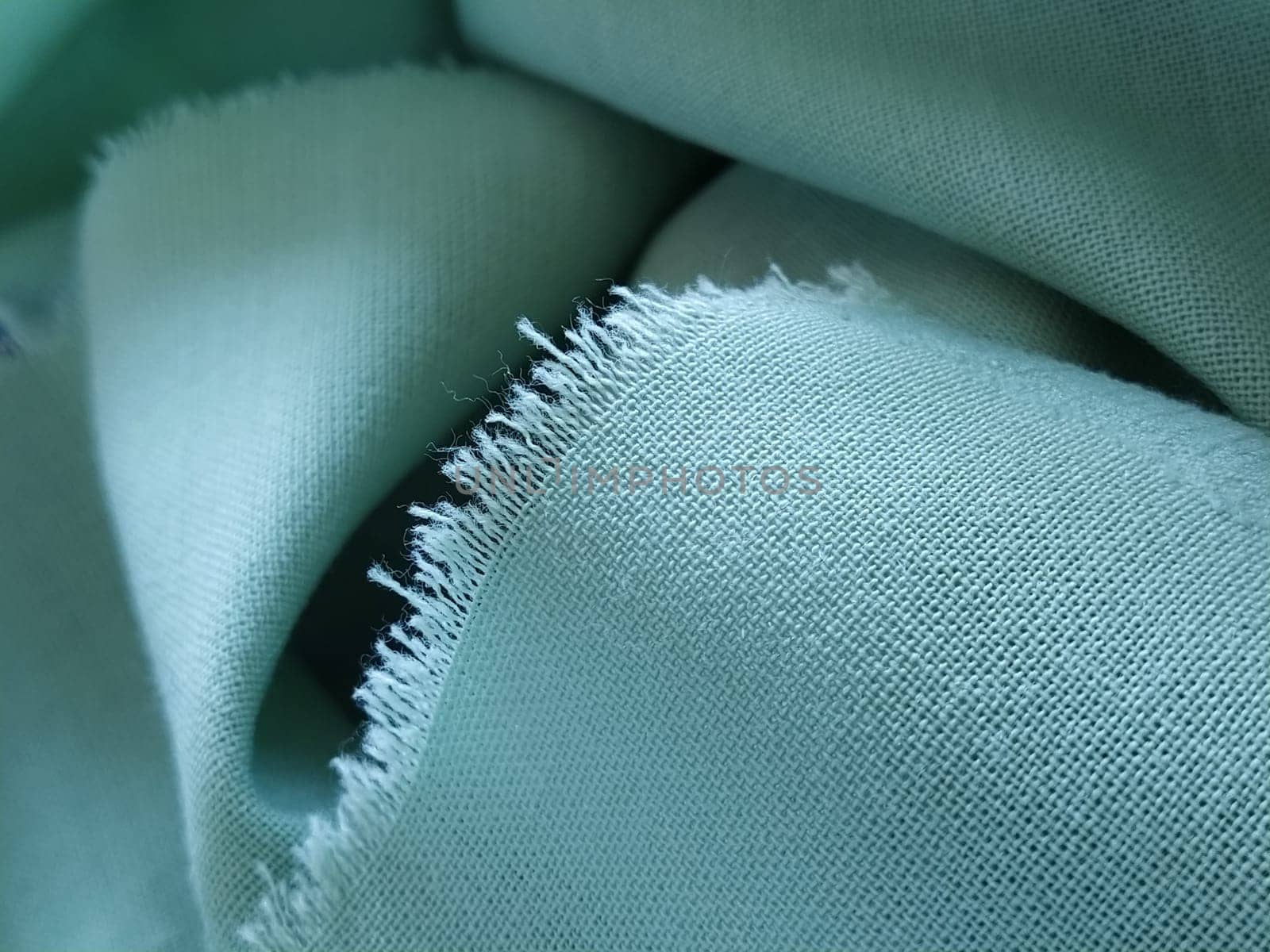 Close up of a woolen fabric of green color. Abstract canvas background, empty template. Thin natural fabric, wool or linen. The edge of the fabric is treated against chapping.