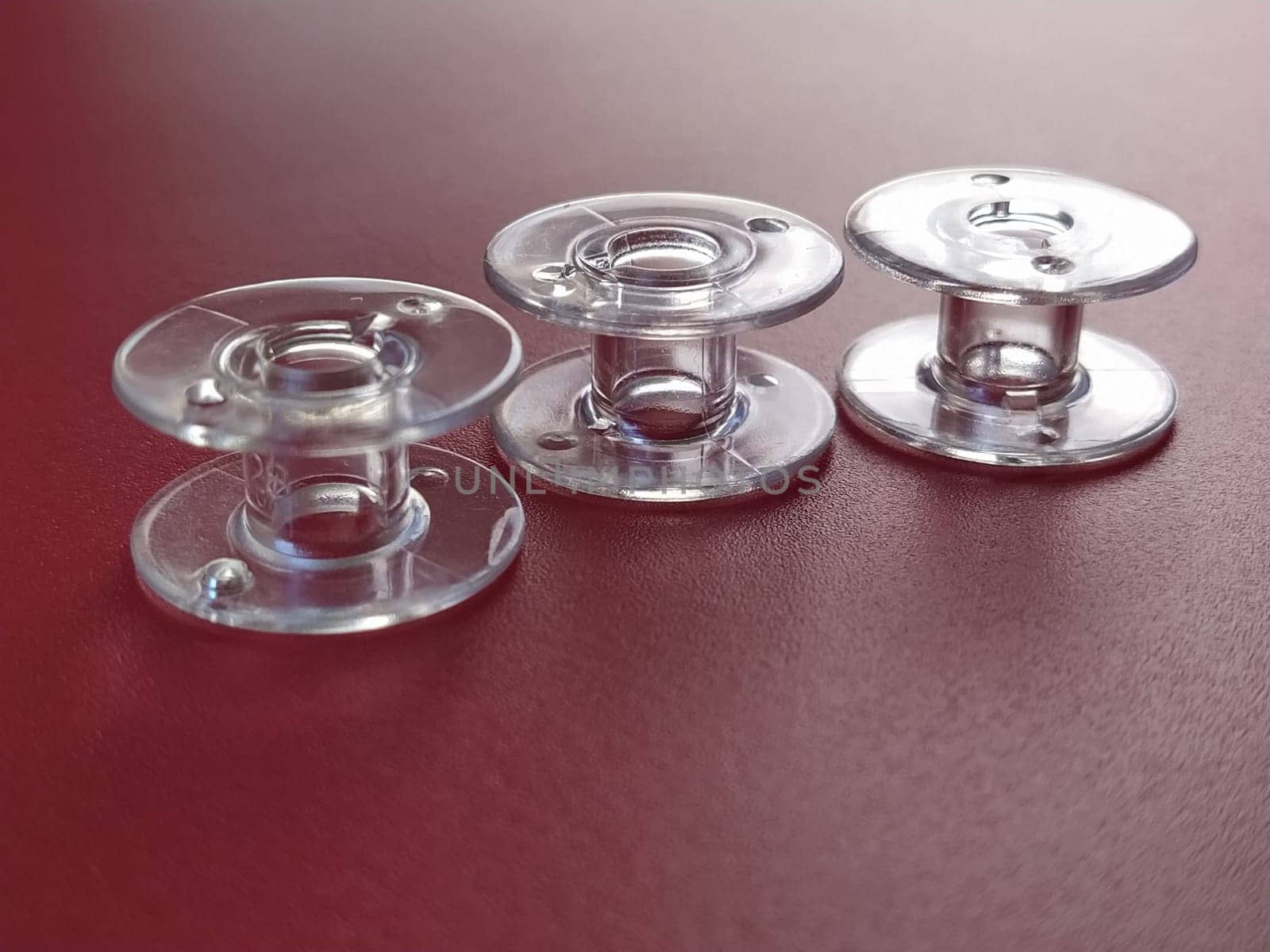 Three transparent plastic sewing machine bobbins. Textile industry. Detail of sewing equipment. Red background, back lighting.