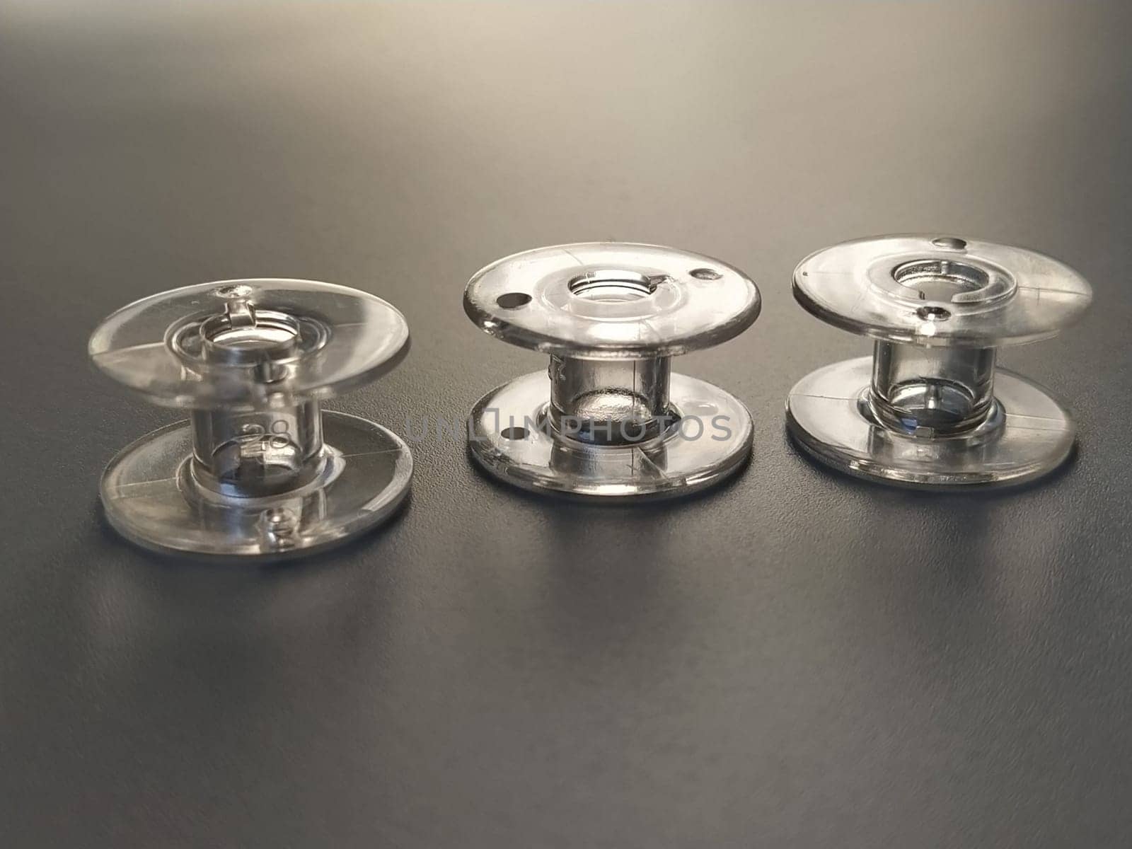 Three transparent plastic sewing machine bobbins. Textile industry. Detail of sewing equipment. Gray background, back lighting.