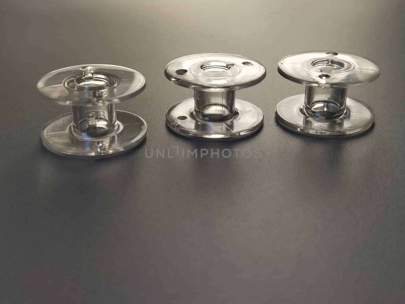 Three transparent plastic sewing machine bobbins. Textile industry. Detail of sewing equipment. Gray background, back lighting.