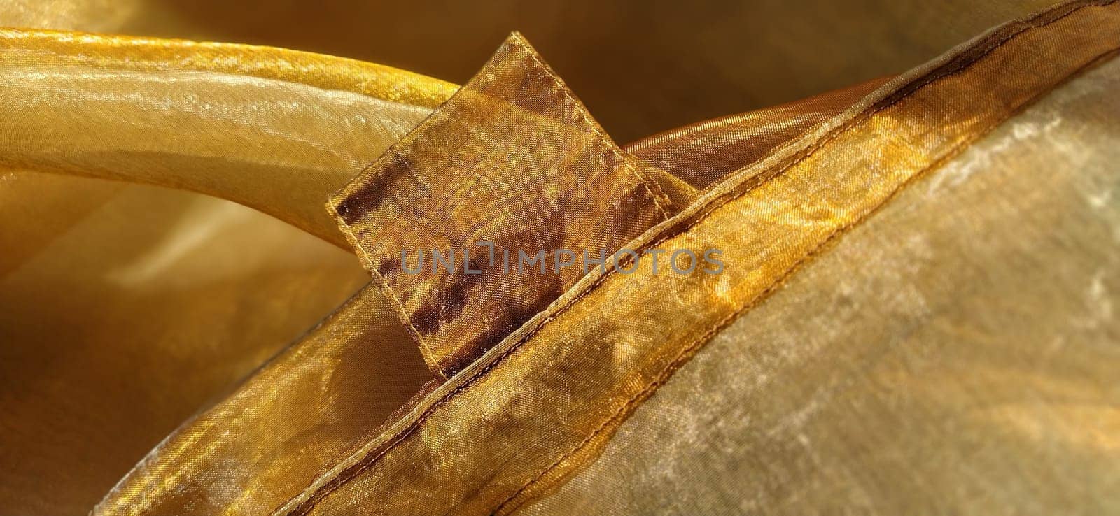 Curtain loops. Beautiful gold fabric. Organza in yellow, orange, beige and brown shades. Pleats in the fabric. Shiny gradient under the light. Folded silky tulle. Transparent curtain material.