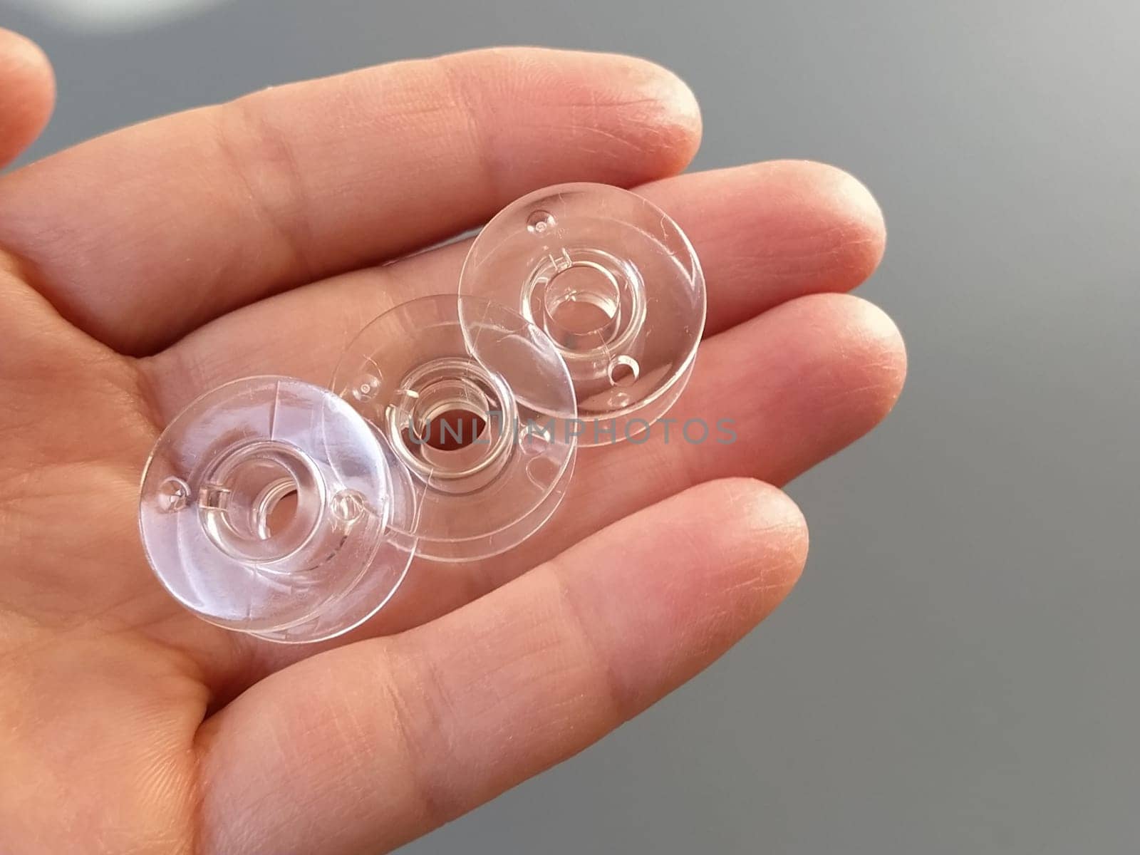 Transparent plastic bobbins from a modern sewing machine in the palm of a woman - a seamstress. Gray background. sewing machines.