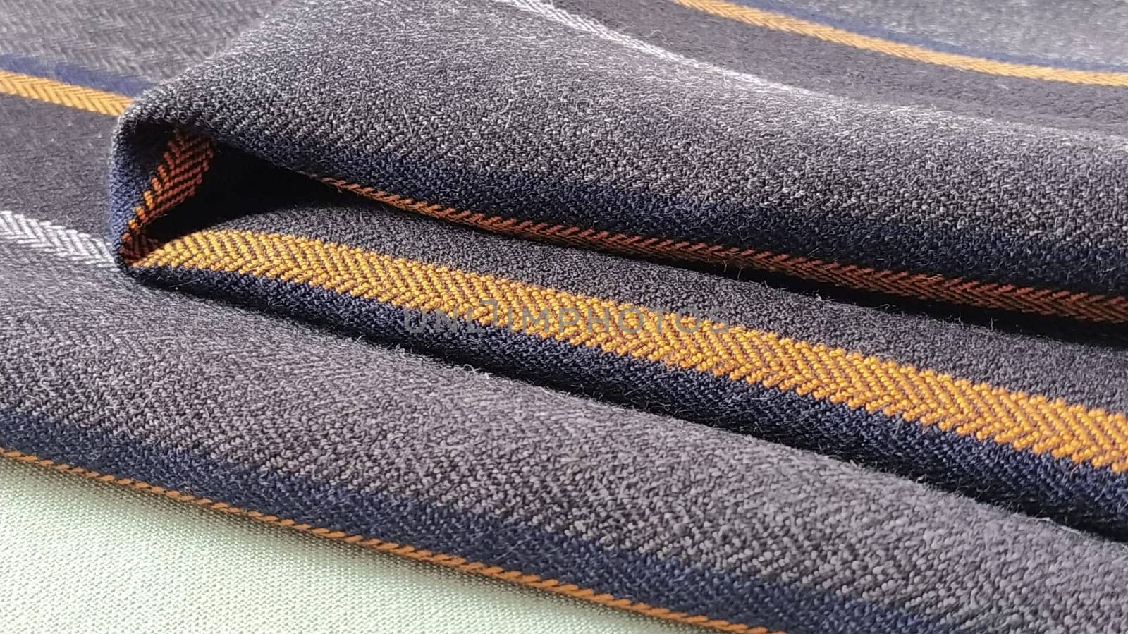 Gray-black fabric with orange and blue stripes. Textile fabric folded neatly on the surface. Natural wool material for sewing clothes and upholstery. Lifestyle. Close-up. Soft focus.