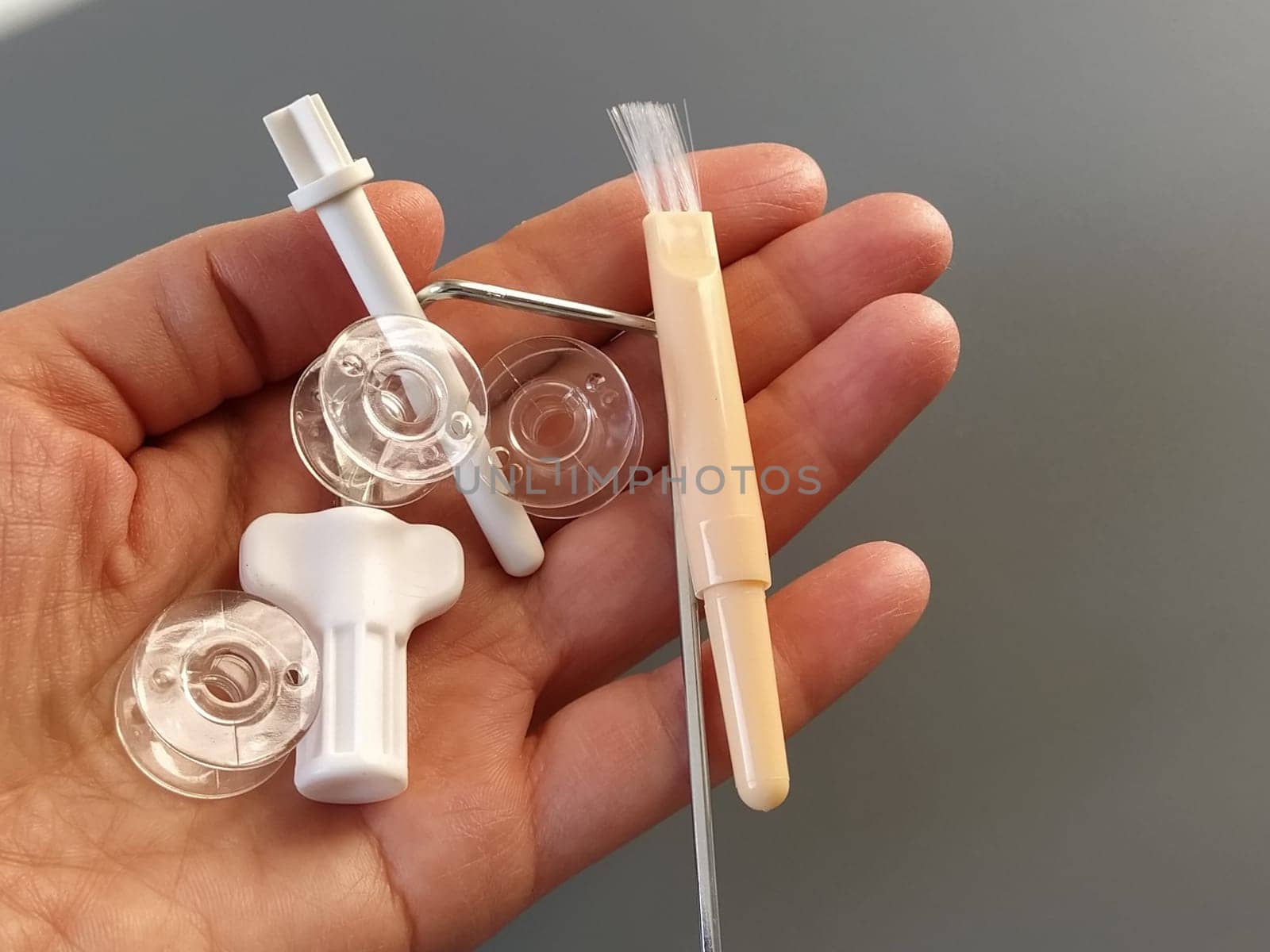 Transparent plastic bobbins from a modern sewing machine in the palm of a woman - seamstresses, needles, thread take-up, whipping tool. Gray background. sewing machines.