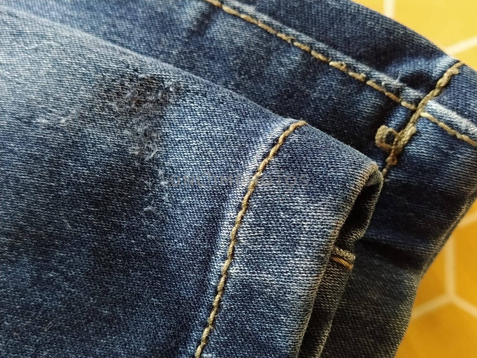 Denim fabric with seams made with red or beige threads close-up. Textile texture. Blue color of the material. Light industry sewing product. Bent and hemmed leg.