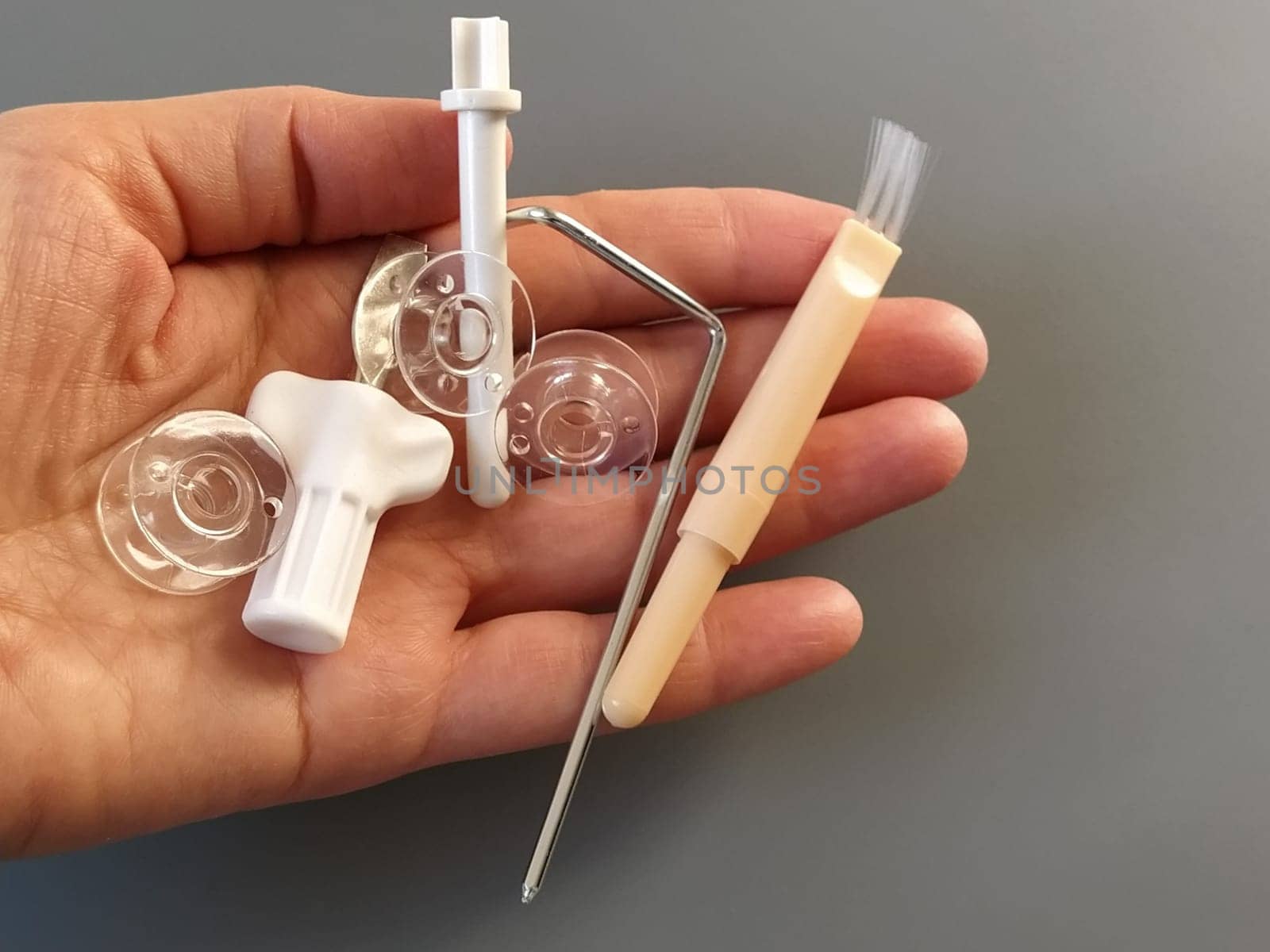 Transparent plastic bobbins from a modern sewing machine in the palm of a woman - seamstresses, needles, thread take-up, whipping tool. Gray background. sewing machines.