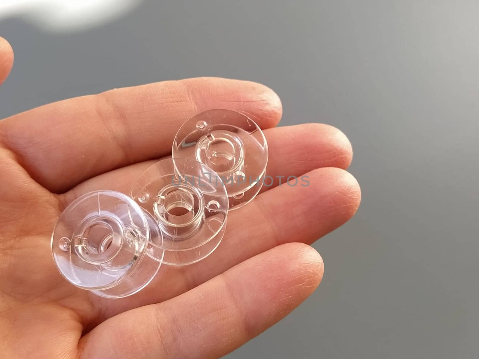 Transparent plastic bobbins from a modern sewing machine in the palm of a woman - a seamstress. Gray background. sewing machines.
