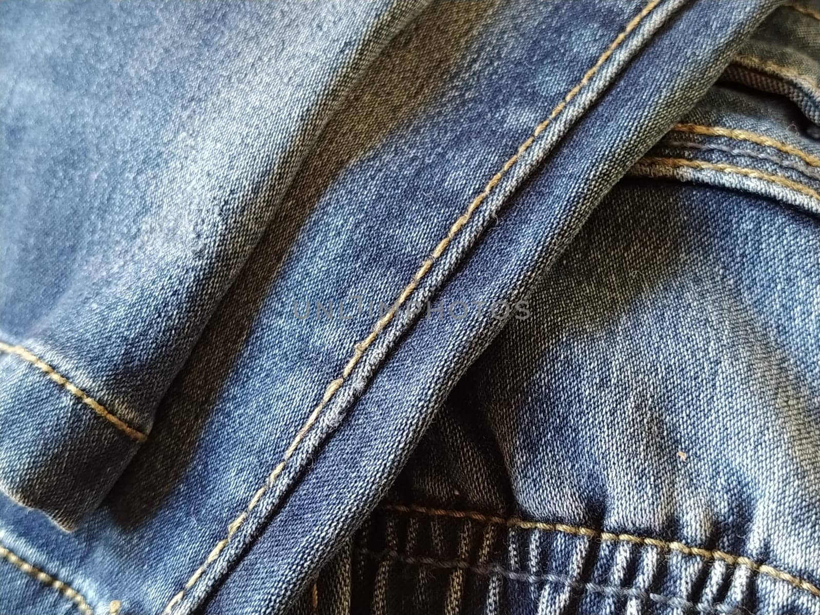 Denim fabric with seams made with red or beige threads close-up. Textile texture. Blue color of the material. Light industry sewing product. Fashion elements on jeans.