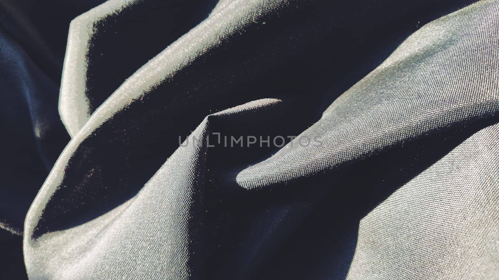 black fabric with interlacing threads close-up. Dark blue tint. Nice beautiful waves on the material. A neatly folded fabric. Interior decoration, sewing clothes and curtains. Textile industry.