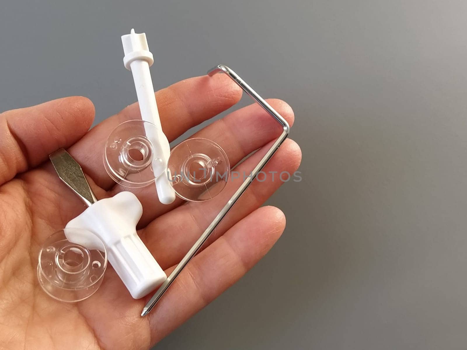 Transparent plastic bobbins from a modern sewing machine in the palm of a woman - seamstresses, needles, thread take-up, whipping tool. Gray background. sewing machines.