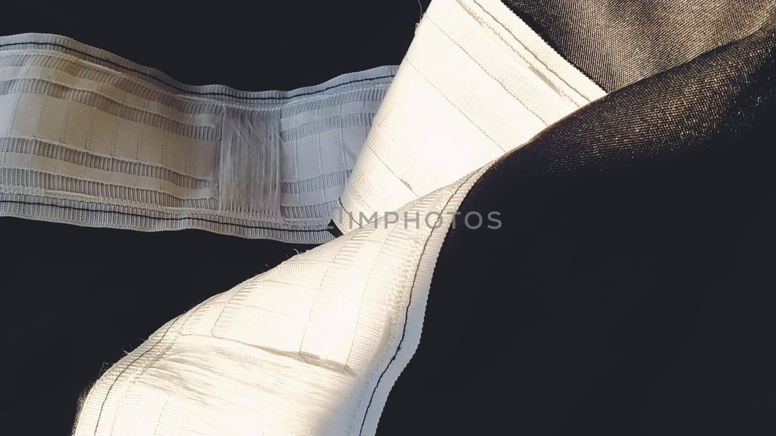 Curtain tape on black curtains. A wide white stripe - a tape for hanging curtains by hooks to the cornice. Home interior. Apartment decor. Light industry.