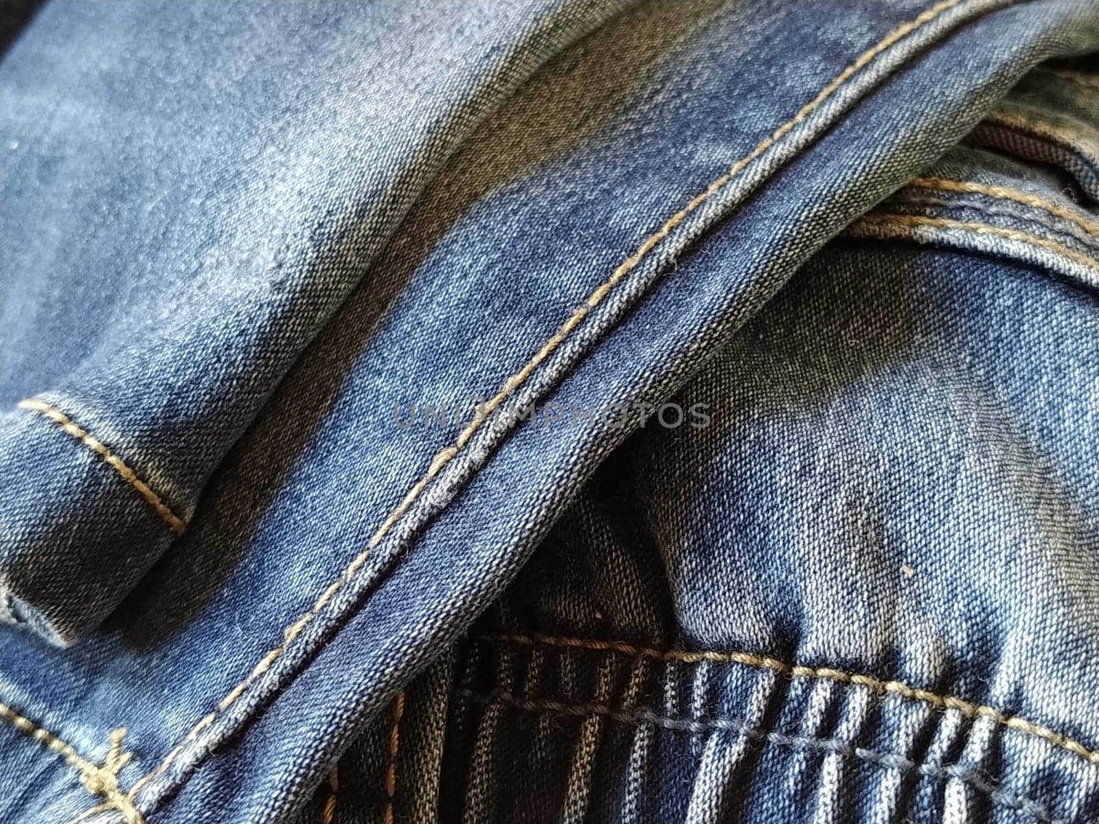 Denim fabric with seams made with red or beige threads close-up. Textile texture. Blue color of the material. Light industry sewing product. Fashion elements on jeans.
