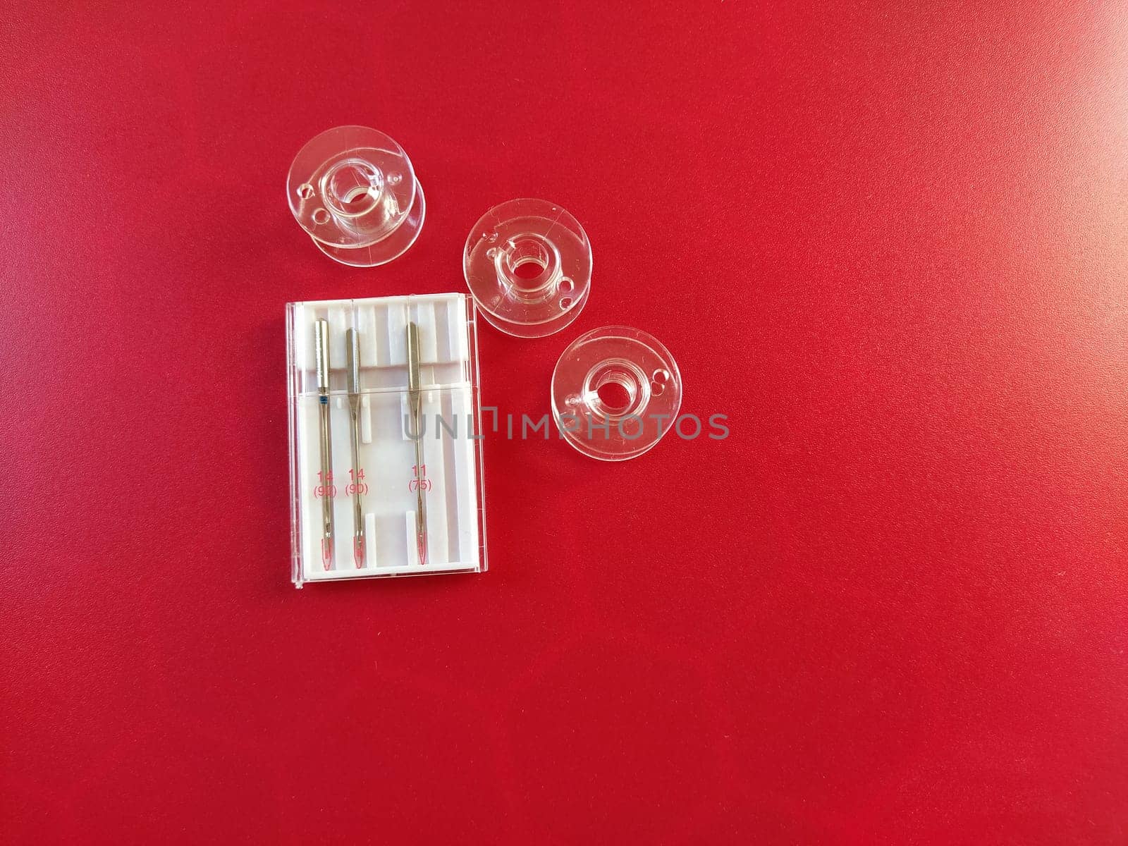 plastic bobbins and a set of sewing machine needles on a red background.