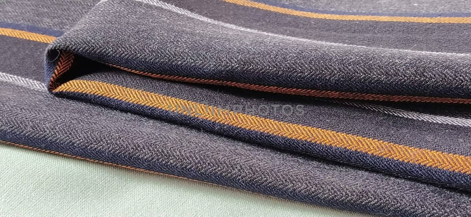 Light green and black-gray folded fabric with orange and dark blue stripes. Interior decoration. Dress fabrics in casual style. Dense material for indoor curtains and furniture finishing.