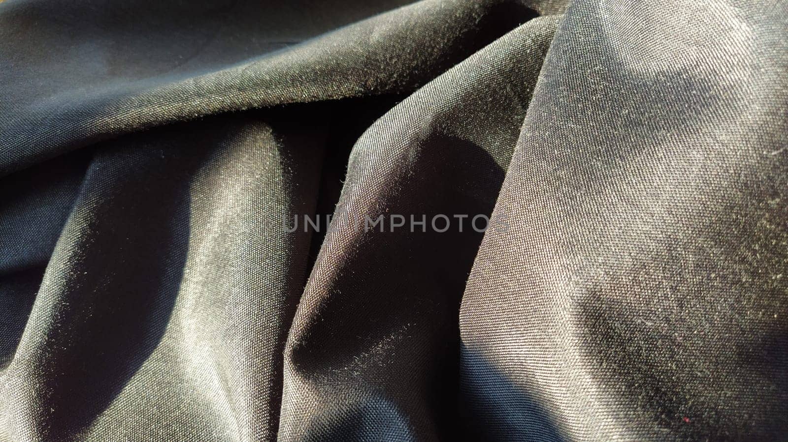 black fabric with interlacing threads close-up. Dark blue tint. Nice beautiful waves on the material. A neatly folded fabric. Interior decoration, sewing clothes and curtains. Textile industry.