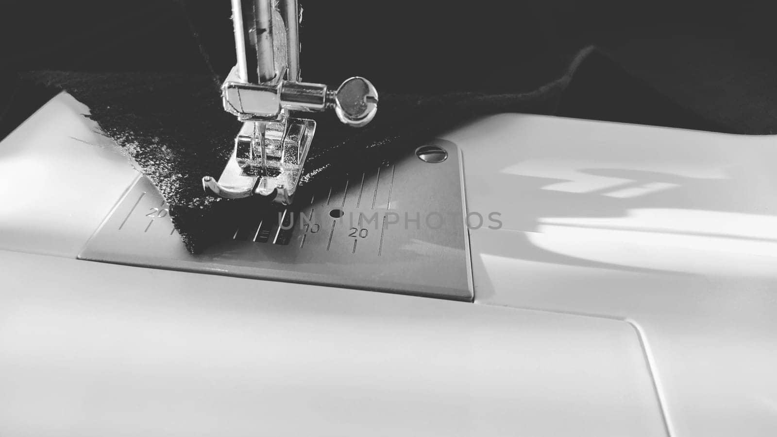 Sewing process on a modern sewing machine, close-up. Sewing machine foot with a needle. Dark blue fabric is trimmed with double wrapping of the fabric edge. Natural sunlight.