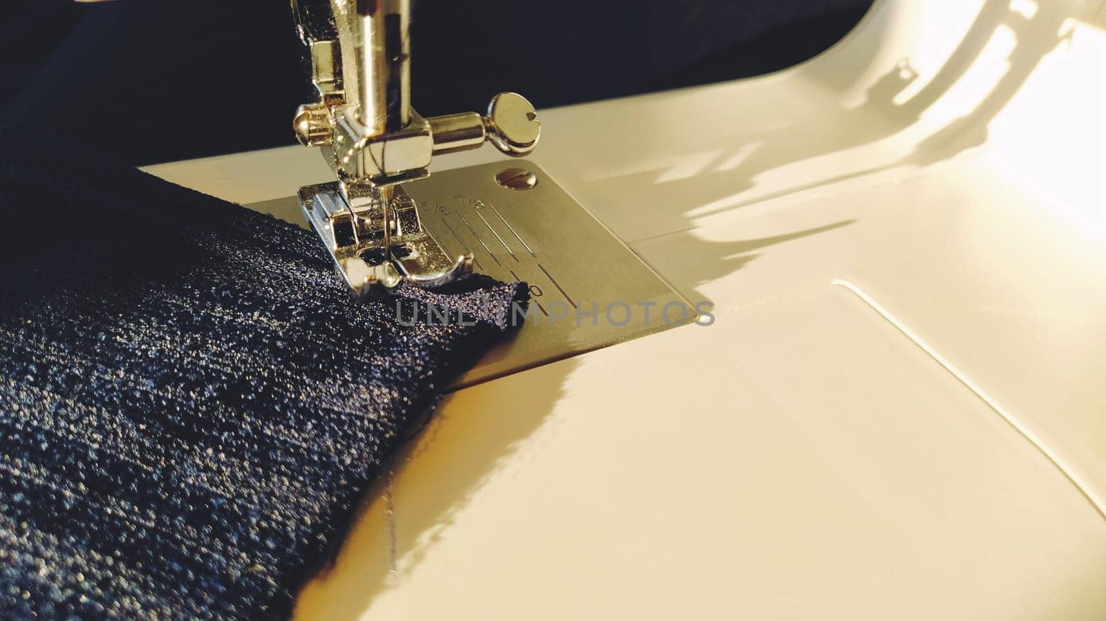 Sewing process on a modern sewing machine, close-up. Sewing machine foot with a needle. Dark blue fabric is trimmed with double wrapping of the fabric edge. Natural sunlight. Copy space.