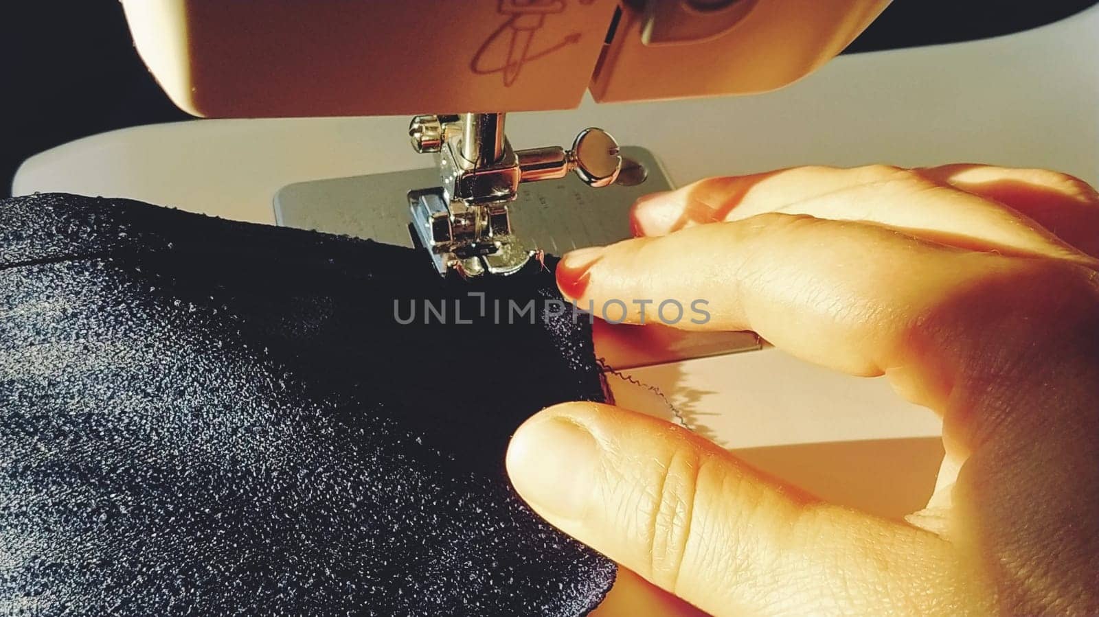 Sewing process on a modern sewing machine, close-up. Sewing machine foot with a needle. Dark blue fabric is trimmed with double wrapping of the fabric edge. Natural sunlight.