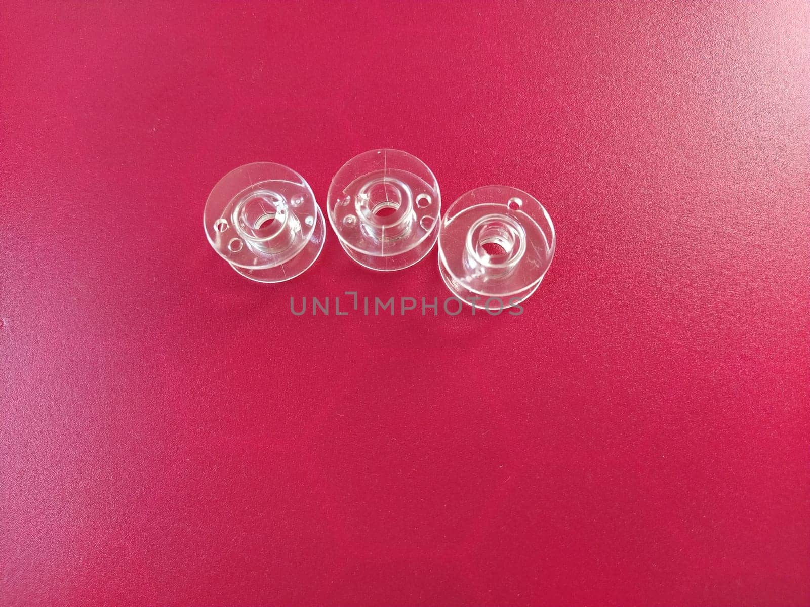 Three transparent plastic sewing machine bobbins. Textile industry. Detail of sewing equipment. Red background.