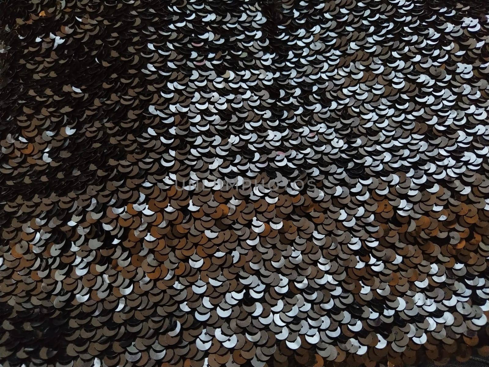 Sequin fabric. Black sequins with white and gray sheen. Reflection of light on individual elements in a chaotic manner. Sewing or Christmas decorative background.