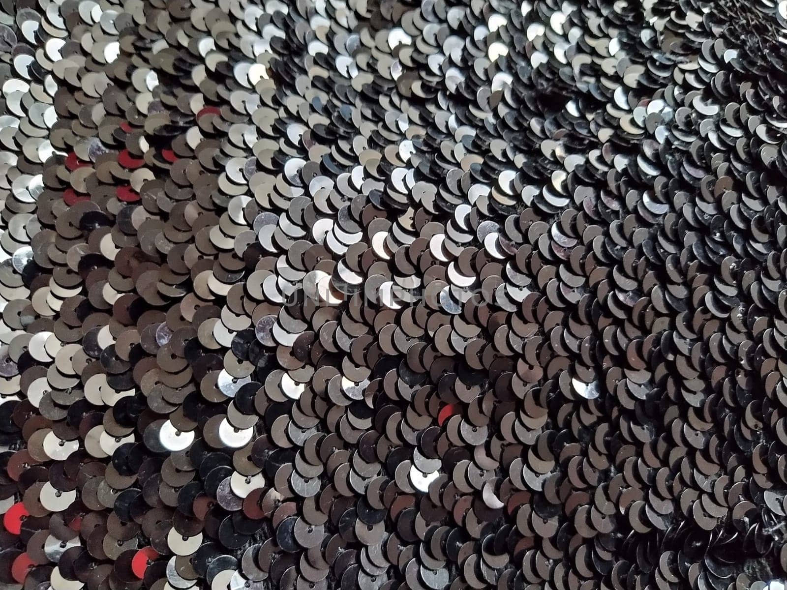 Sequin fabric. Black sequins with white and gray sheen. Reflection of light on individual elements in a chaotic manner. Sewing or Christmas decorative background.