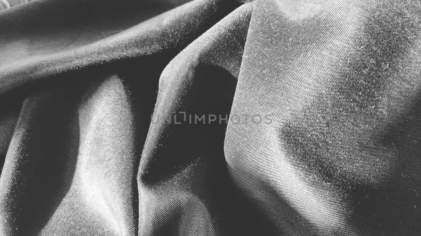 black fabric with interlacing threads close-up. Black and white monochrome photography. Nice beautiful waves on the material. Folded fabric. Interior decoration, sewing clothes and curtains. Textile