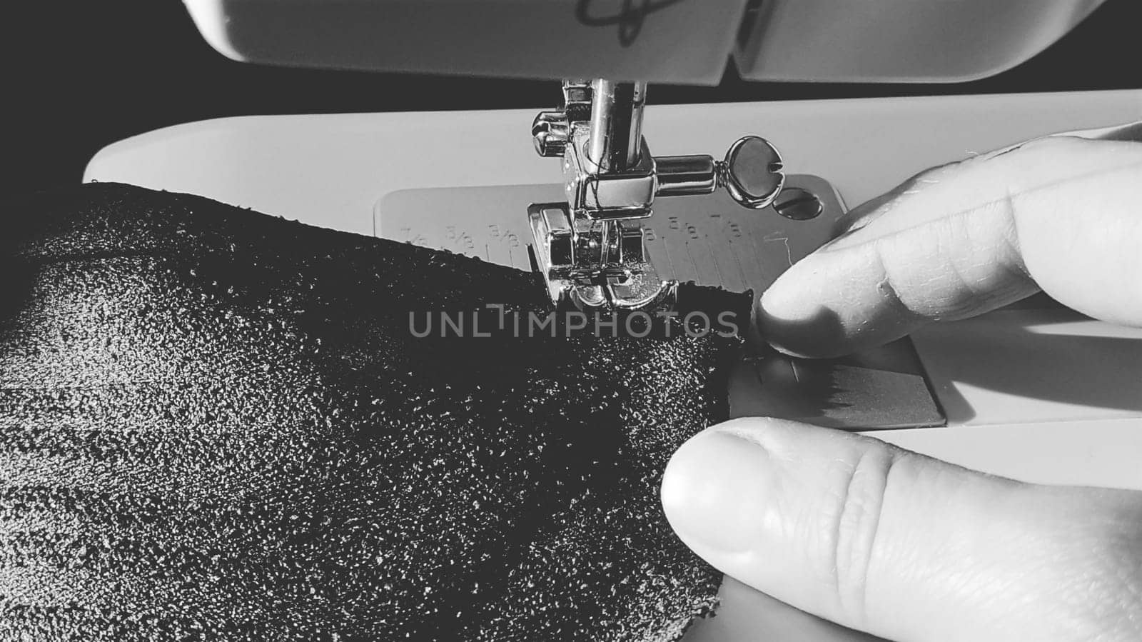 Sewing process on a modern sewing machine, close-up. Sewing machine foot with a needle. Dark blue fabric is trimmed with double wrapping of the fabric edge. Natural sunlight.