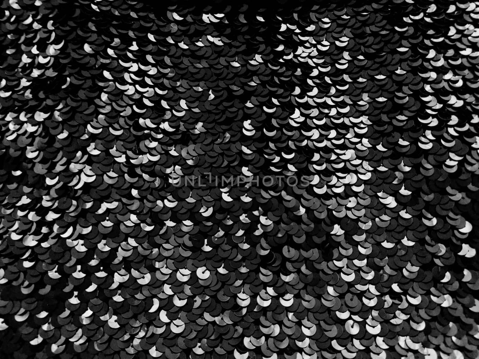 Sequin fabric. Black sequins with white and gray sheen. Reflection of light on individual elements in a chaotic manner. Sewing or Christmas decorative background.
