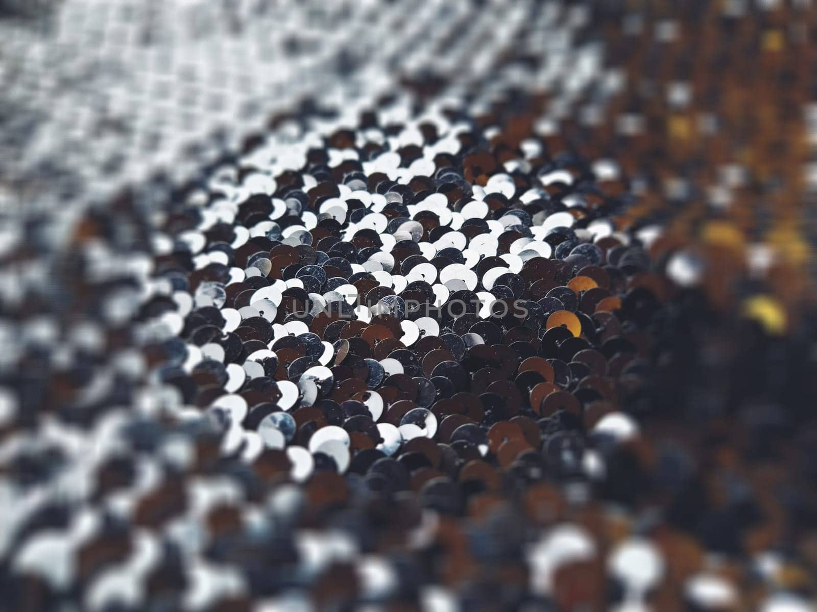 Sequin fabric. Black sequins with white-gray tint. Reflection of light on individual elements in a chaotic manner. Blurred circle background. Soft focus.