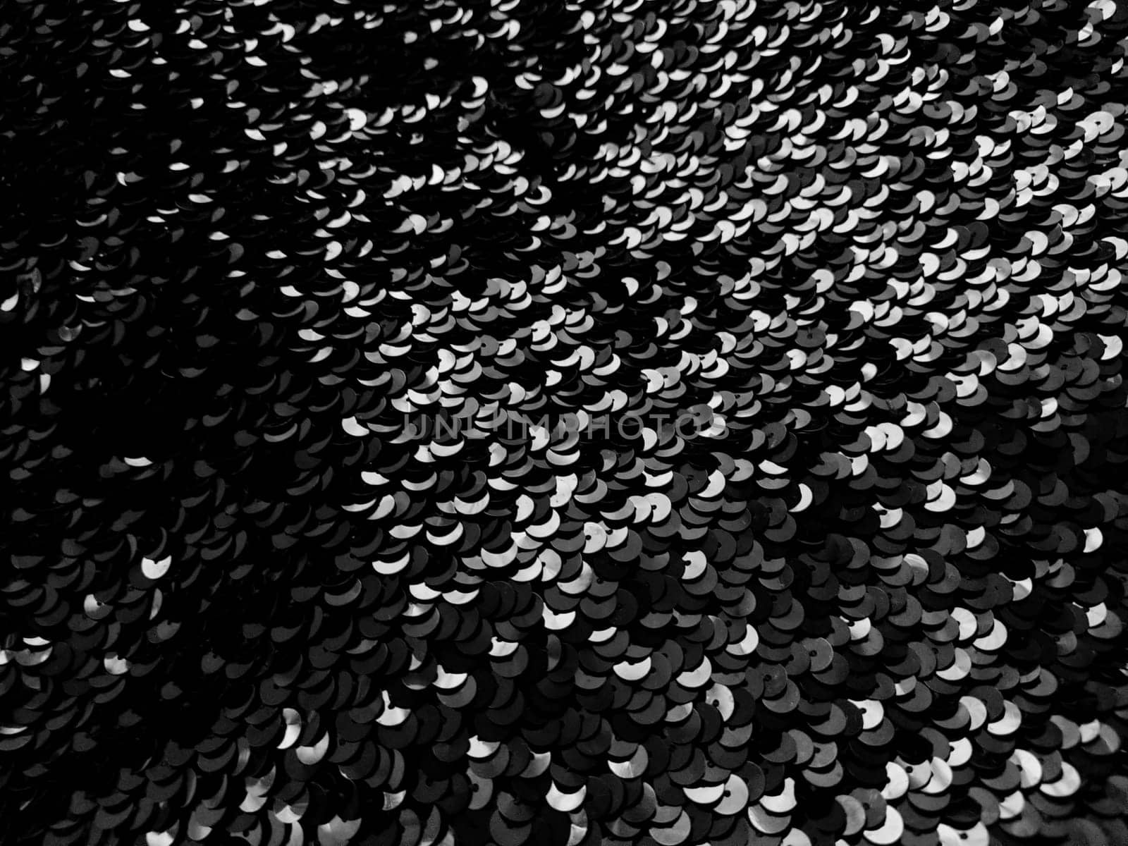 Sequin fabric. Black sequins with white and gray sheen. Reflection of light on individual elements in a chaotic manner. Sewing or Christmas decorative background.