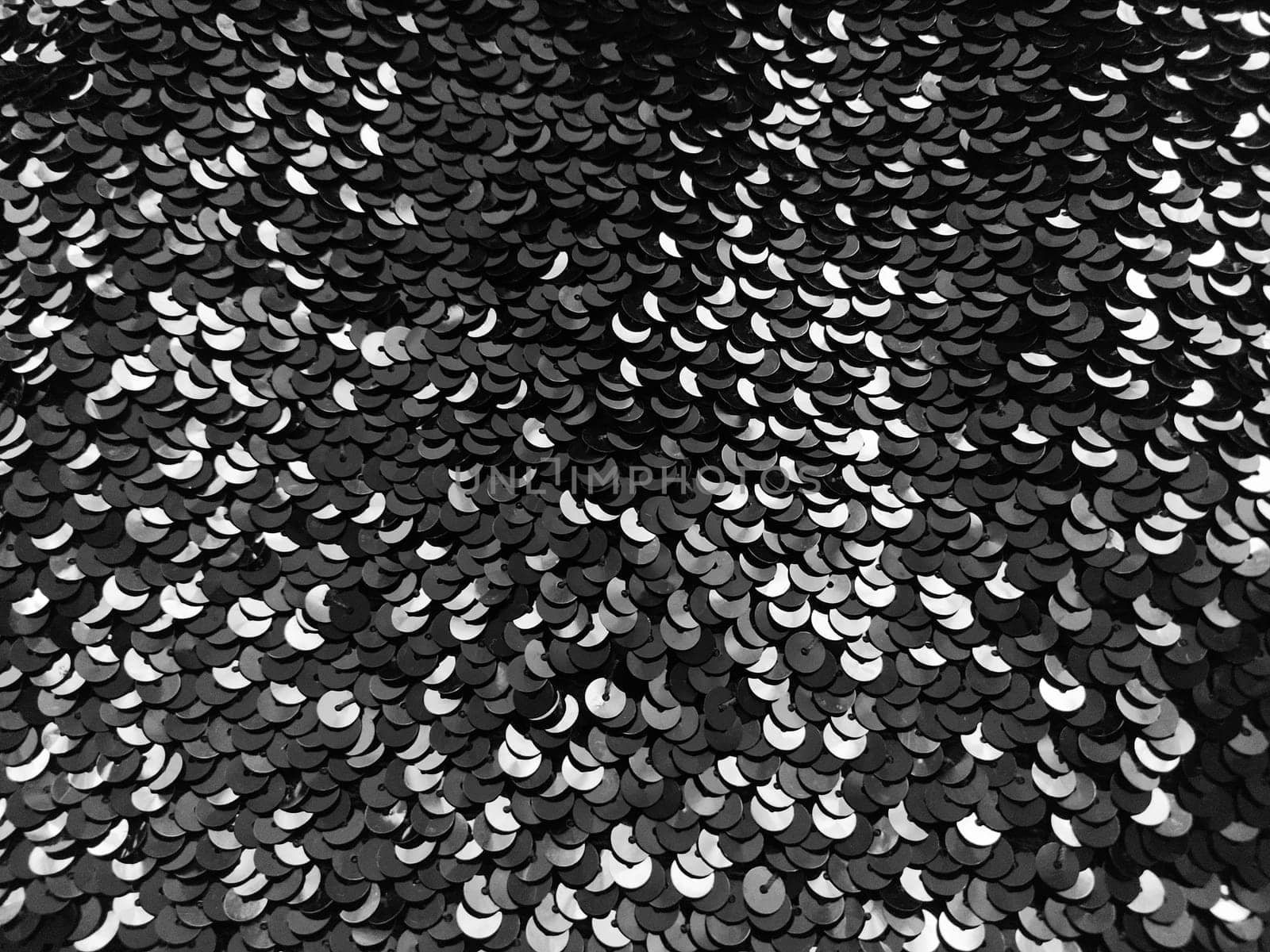 Sequin fabric. Black sequins with white and gray sheen. Reflection of light on individual elements in a chaotic manner. Sewing or Christmas decorative background.