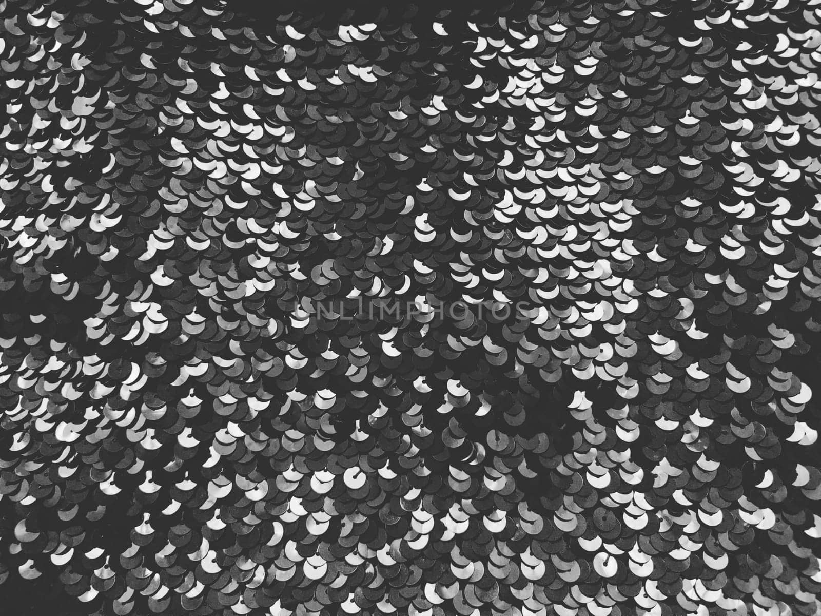 Sequin fabric. Black sequins with white and gray sheen. Reflection of light on individual elements in a chaotic manner. Sewing or Christmas decorative background.