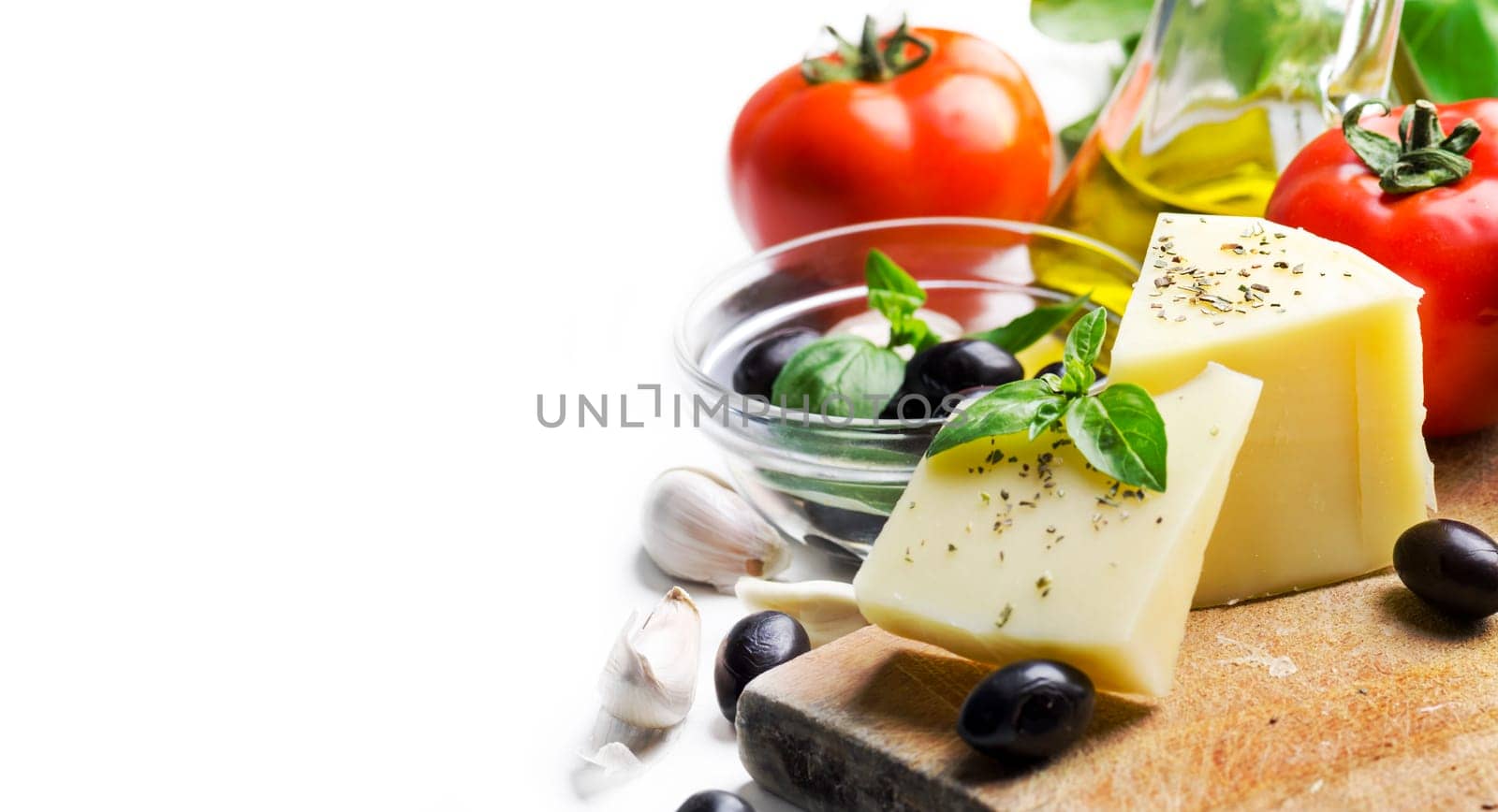 Goat cheese, olives, olive oil, tomato, garlic, basil and spices on wooden cutting board isolated on white background. Food ingredients for italian pizza recipe. Mediterranean cuisine with dairy product and organic vegetable and herbs.