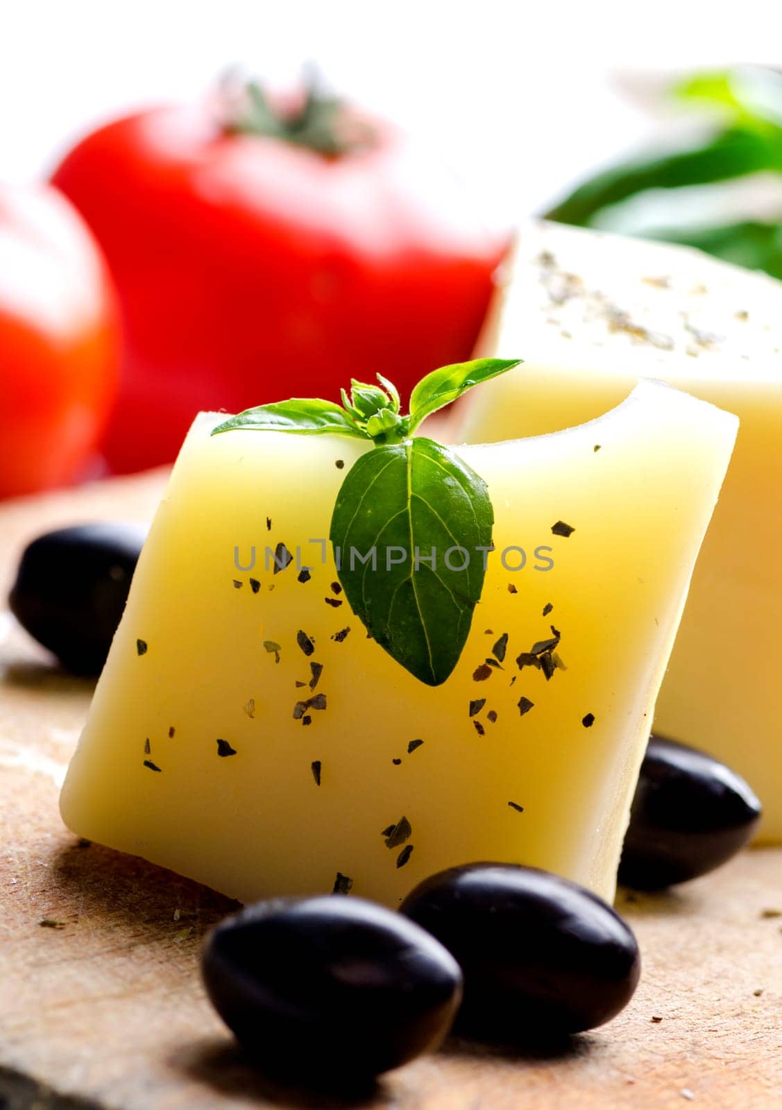 Closeup of goat cheese, olives, fresh tomato, basil and spices on wooden cutting board. Food ingredients for italian pizza recipe. Mediterranean cuisine with dairy product and organic vegetable and herbs.