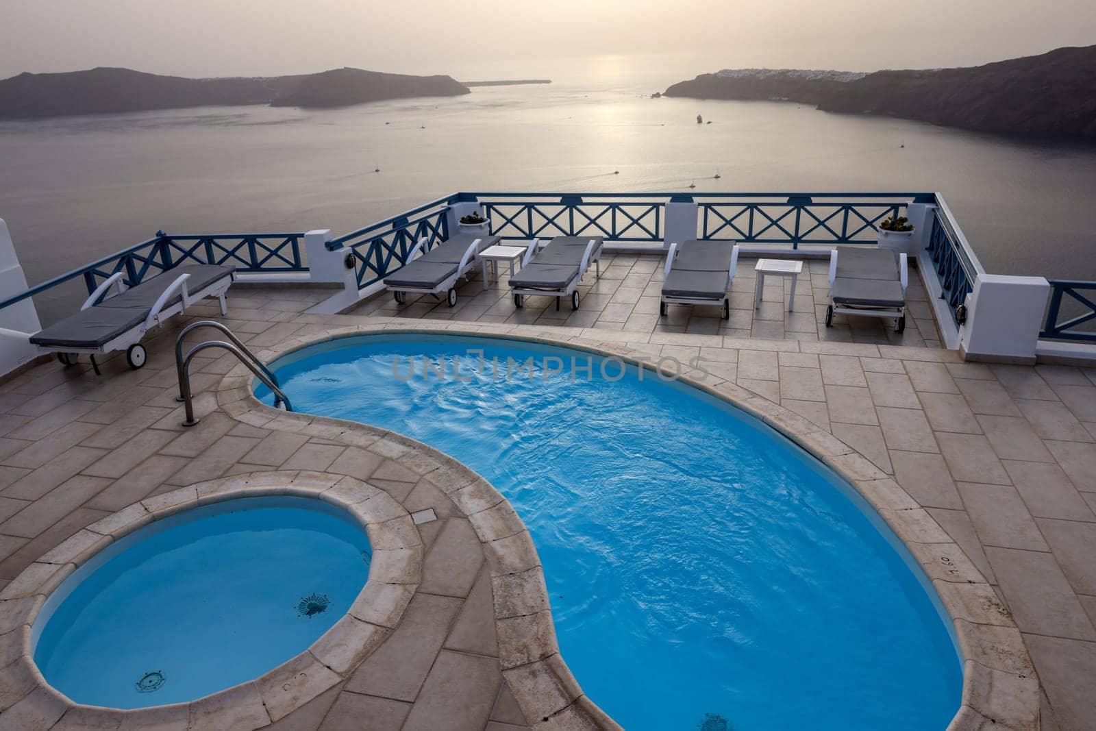 Sun loungers and pools on terrace in the village of Imerovigli with amazing view of sunset over caldera in Santorini. Greece