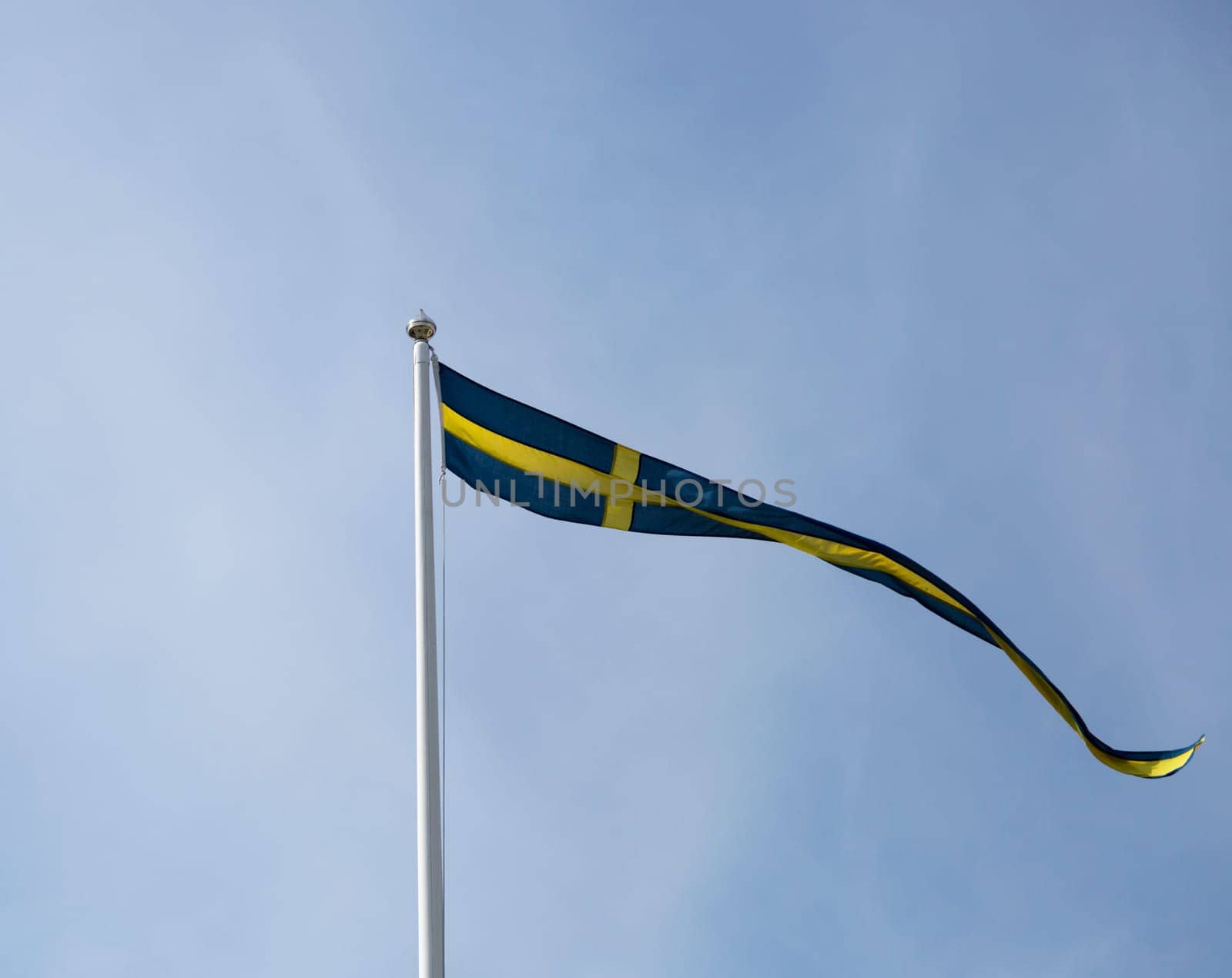 Swedish Pennent Waving on Flagpole with blue sky behing it.