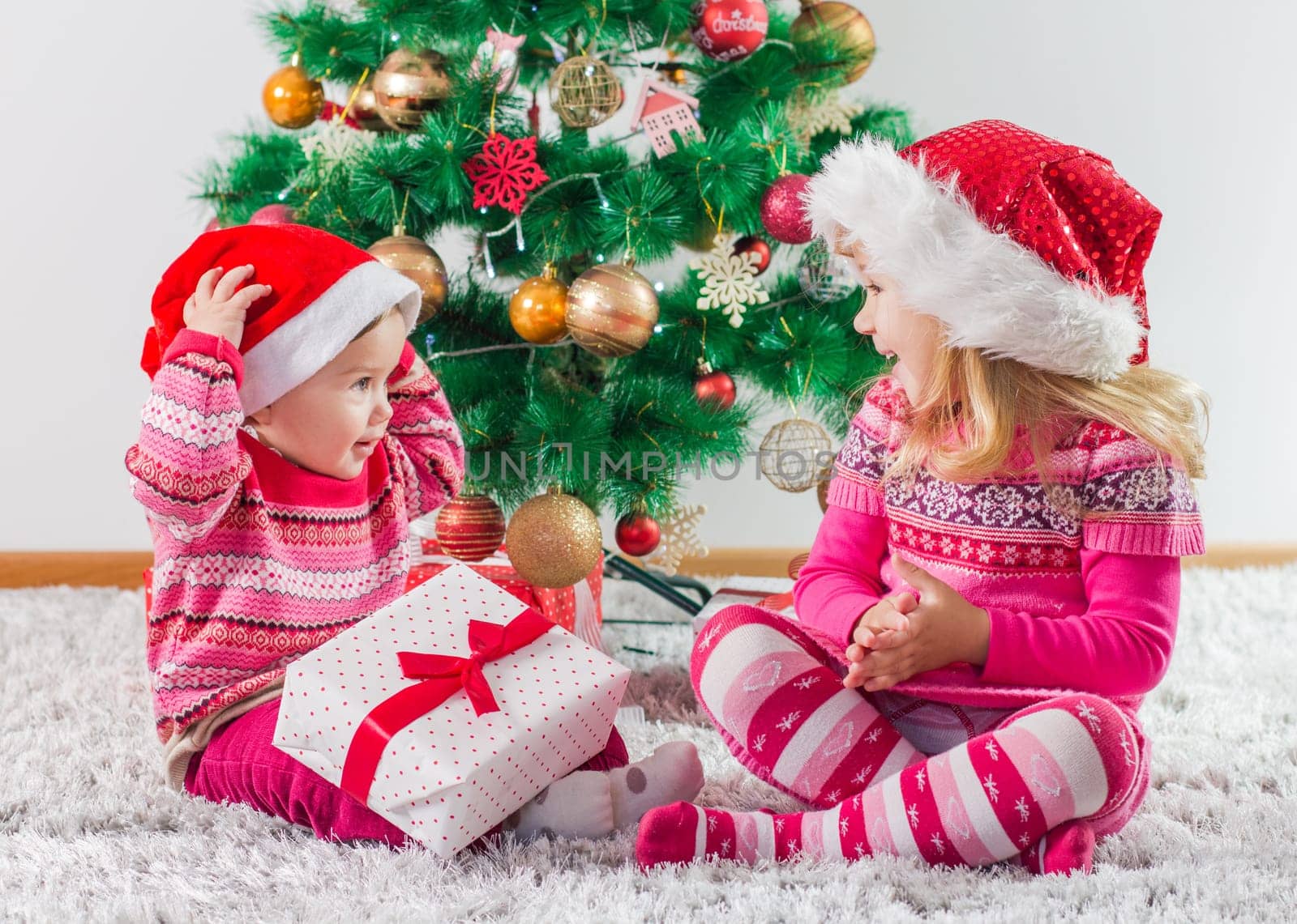 Happy children open Christmas presents on the floor and tree with New Year decoration at home.