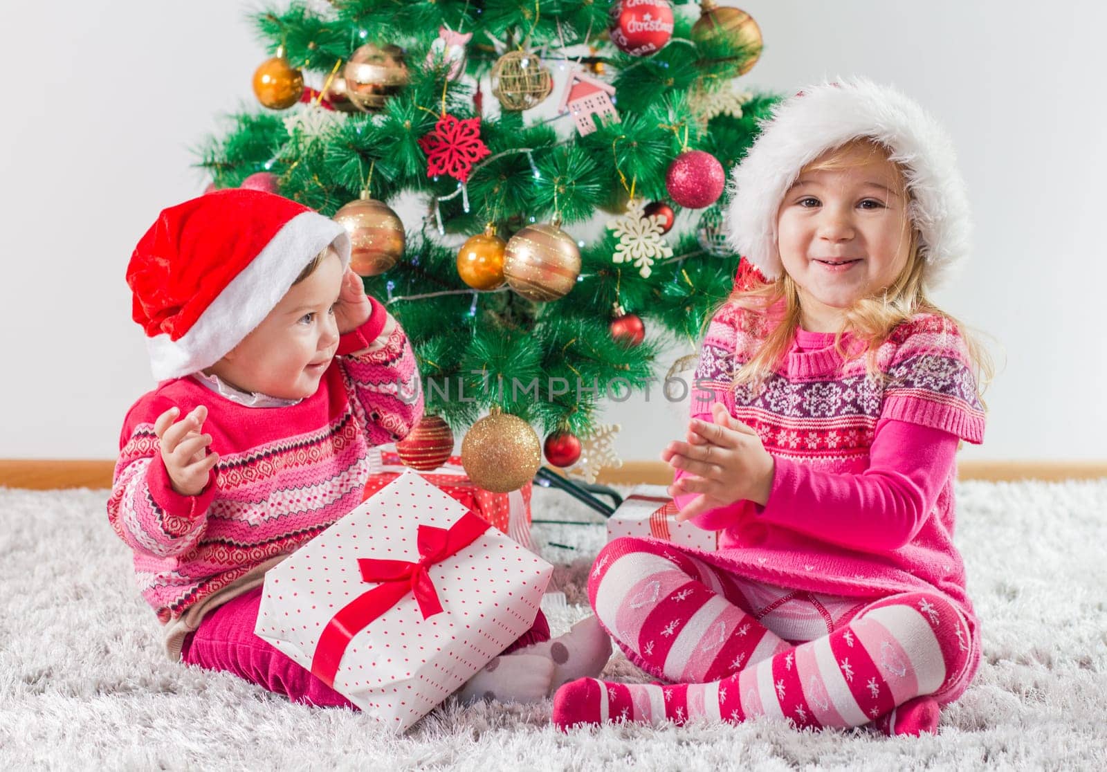 Happy children open Christmas presents on the floor and tree with New Year decoration at home.